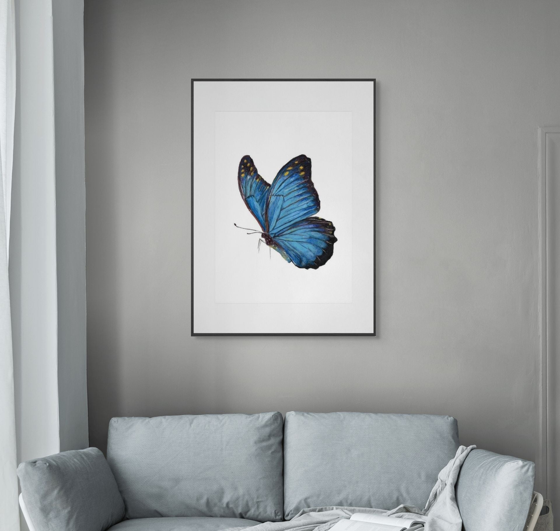 Framed artwork of a blue butterfly on a gray wall above a light gray sofa.