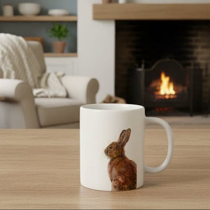 White mug with a rabbit design on a wooden table in a cozy living room with a fireplace.